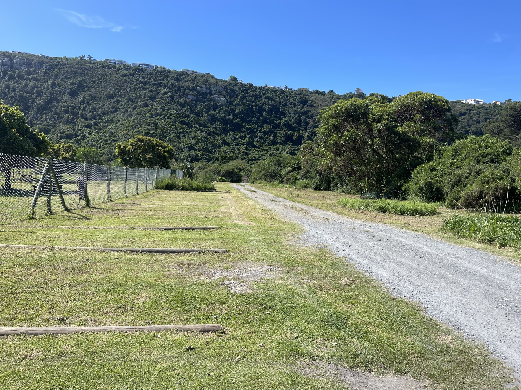 The Happy Place car park beside the fenced enclosure, with a gravel driveway and green hills beyond